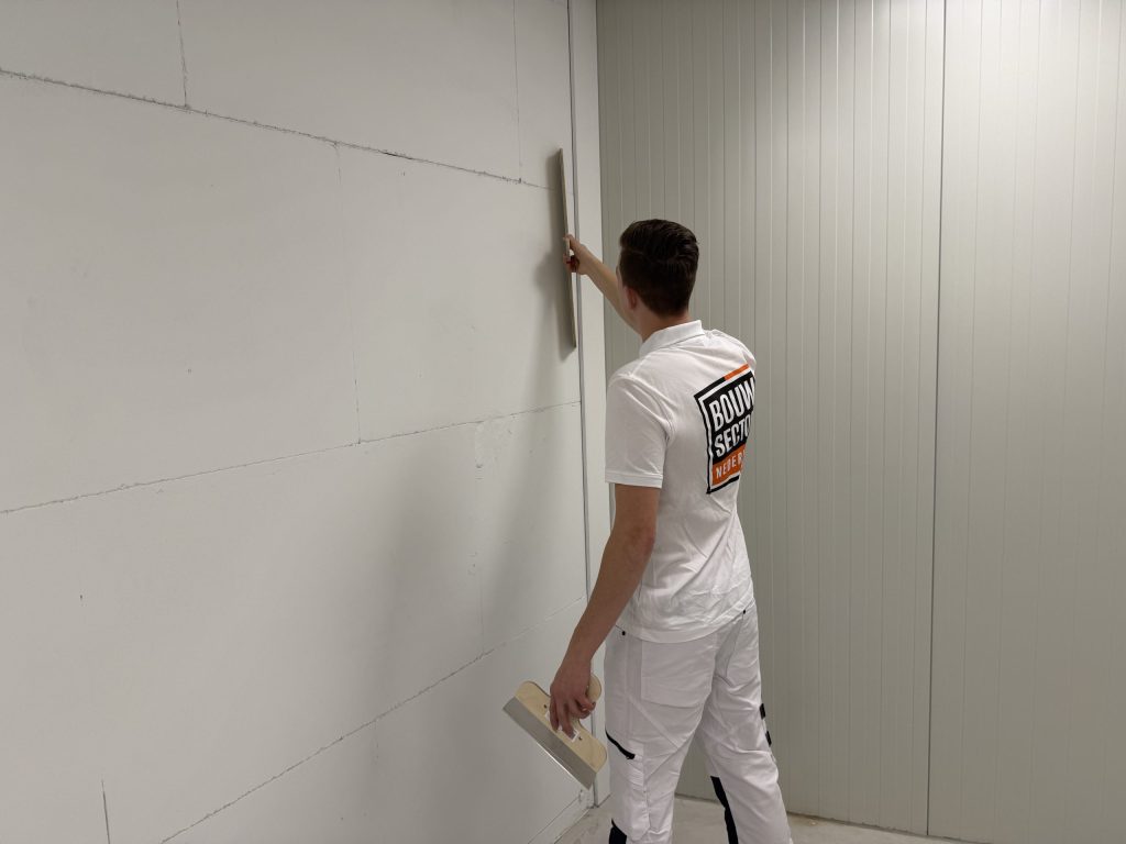 Stukadoor van Bouwsector Nederland trekt een wand met plaatnaden vlak met een lange spaan
