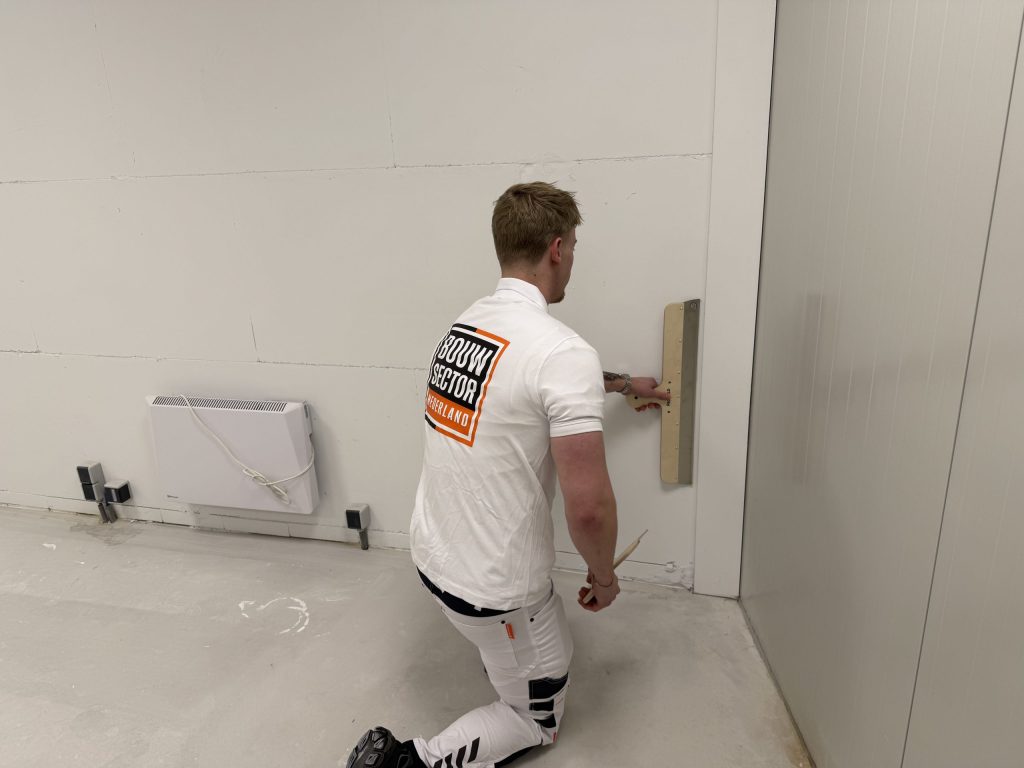Stukadoor van Bouwsector Nederland zit op een knie en maakt het onderste stuk van een muur glad