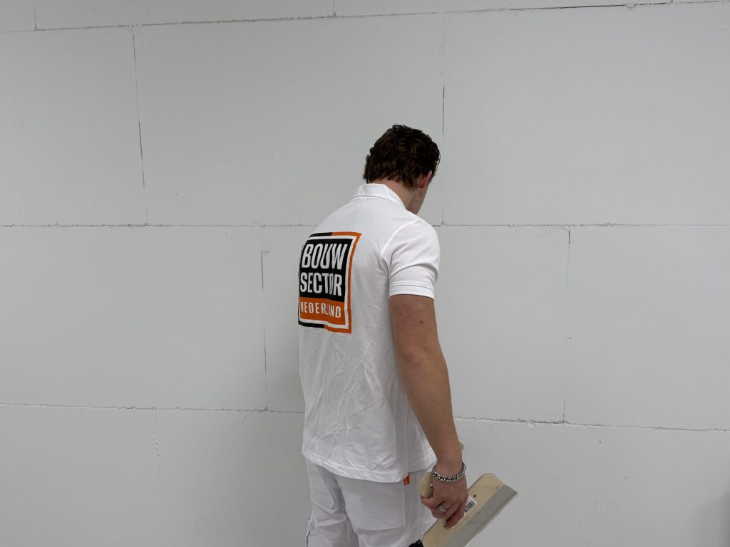 Stukadoor van Bouwsector Nederland staat met een plakspaan voor een kale wand met plaatnaden