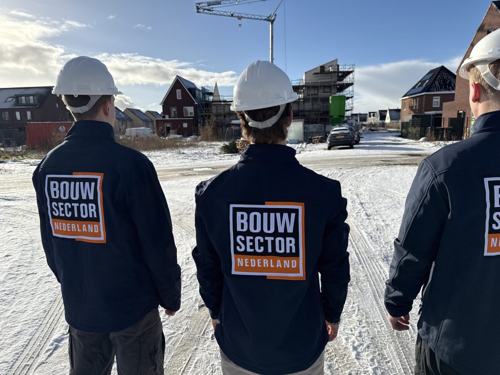 Drie vakmensen van Bouwsector Nederland met witte helm voor huizen in aanbouw op een besneeuwd terrein