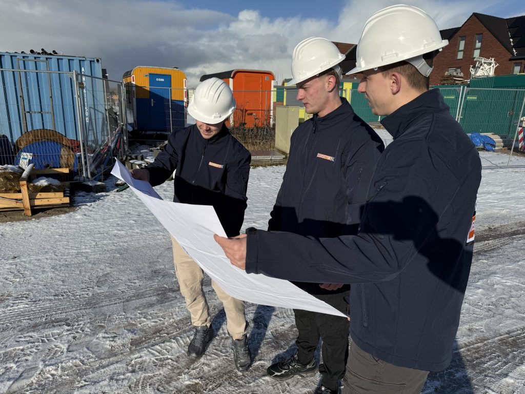 Drie vakmensen van Bouwsector Nederland met witte helm bekijken samen een bouwtekening op de bouwplaats